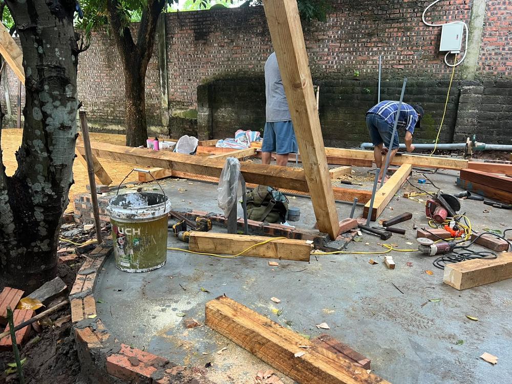 Timber frame of the Garden Laboratory under construction, with a builder steadying an upright post against a brick wall