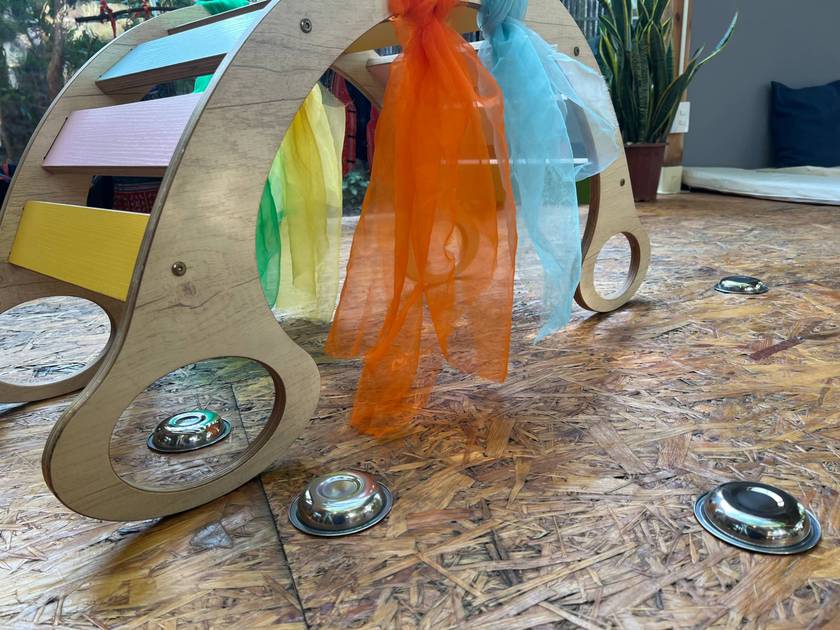 Wooden climbing arch with pastel rungs and silk scarves, above steel bowls on the floor